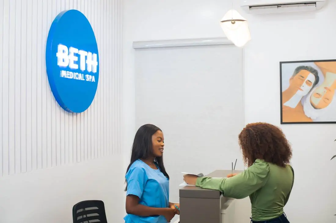 A staff member in blue scrubs assisting a client at the front desk of Beth Beauty Aesthetic Institute